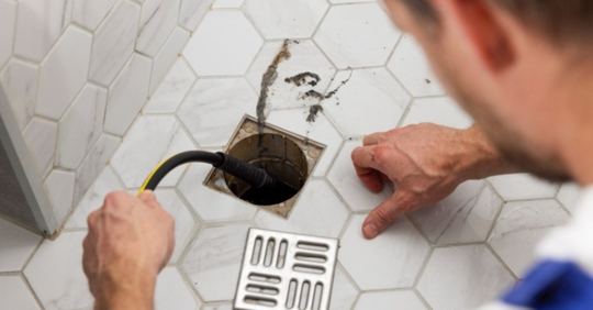 Plumber unclogging blocked shower drain with hydro jetting at home bathroom